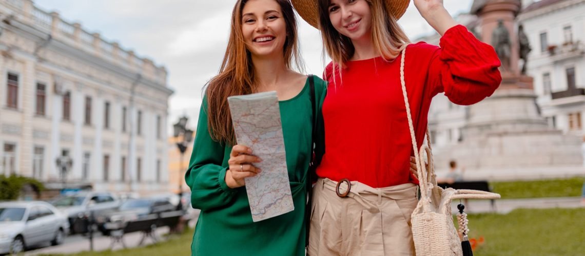 stylish young women traveling together in Europe dressed in spring trendy outfit and accessories smiling happy friends having fun holding map